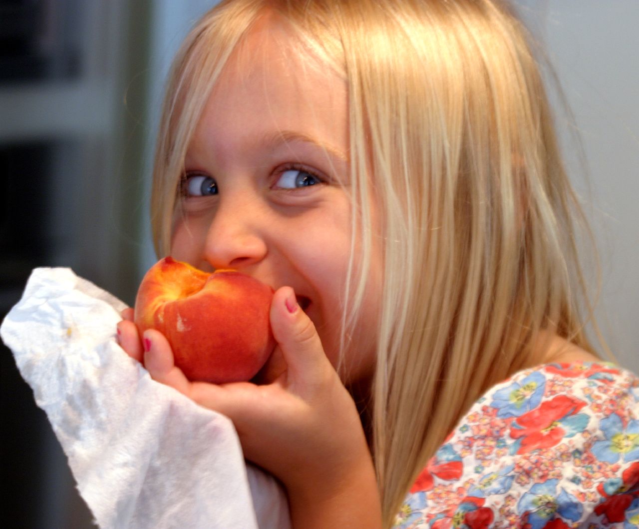 A little girl eating a peach and smiling (Bruce Tuten/Flickr)